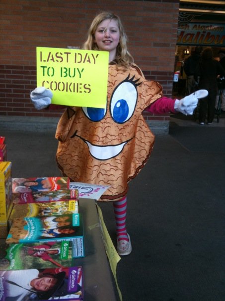 Zoe dressed like a girl scout cookie, holding a sign that says 'Last Day To Buy Cookies'