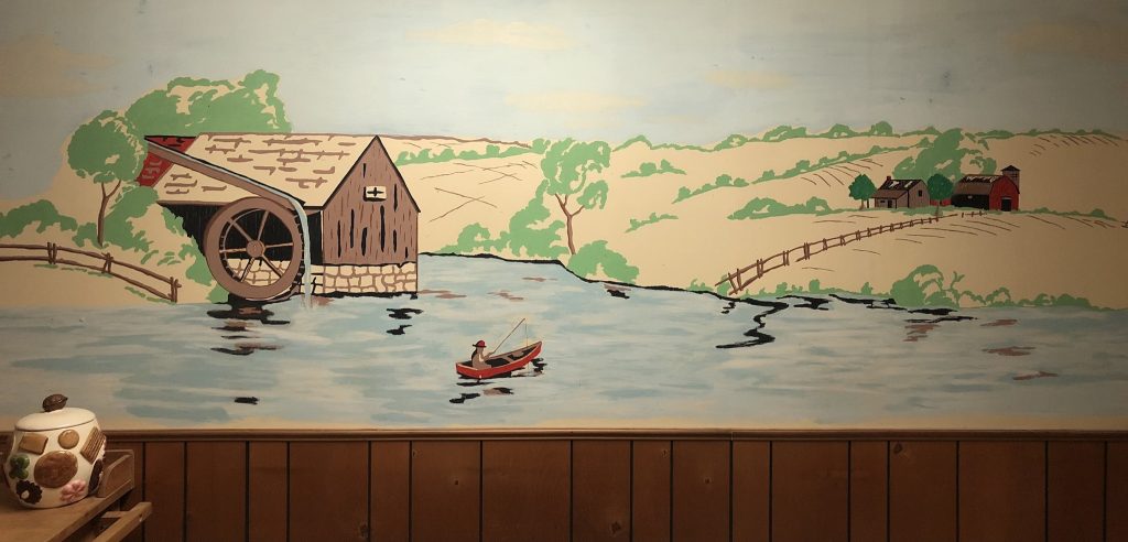 A mural of a fisherman on a lake, surrounded by hills, a barn and a farmhouse