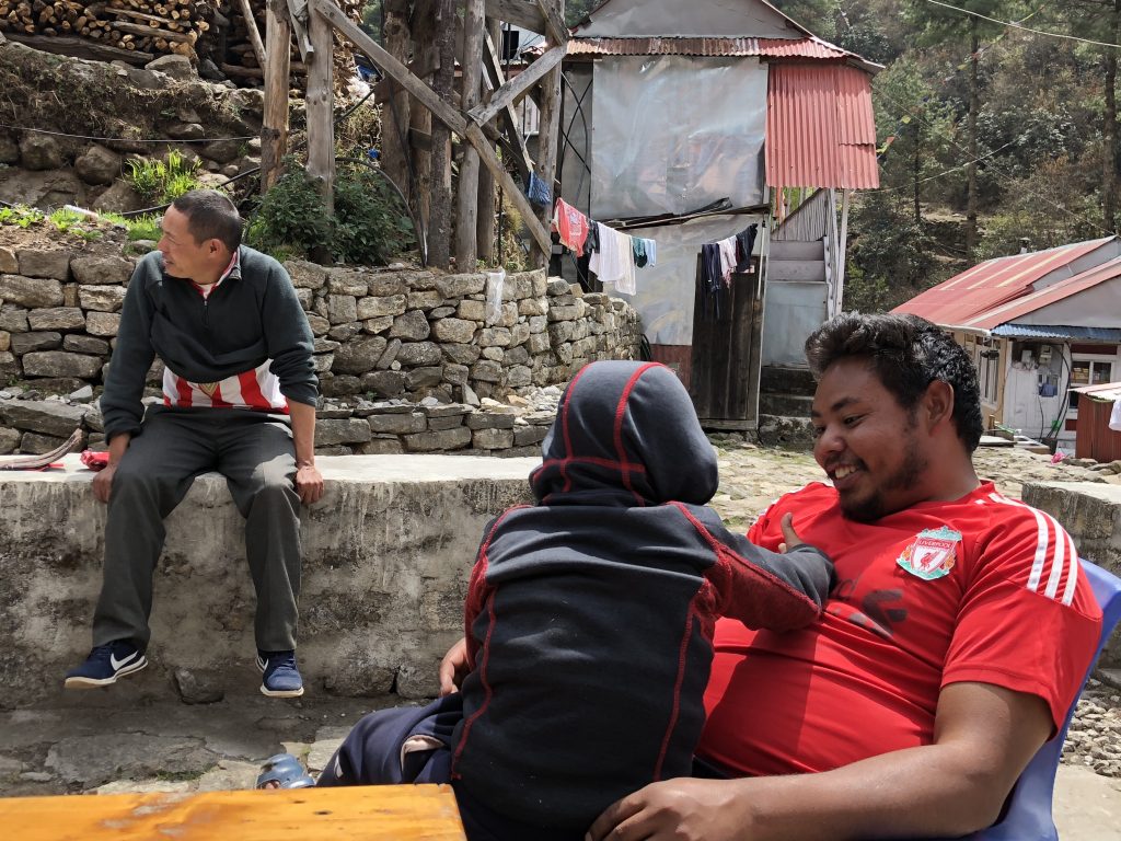 My guide and porter relax in a small village; a small boy leaps into my guide's lap