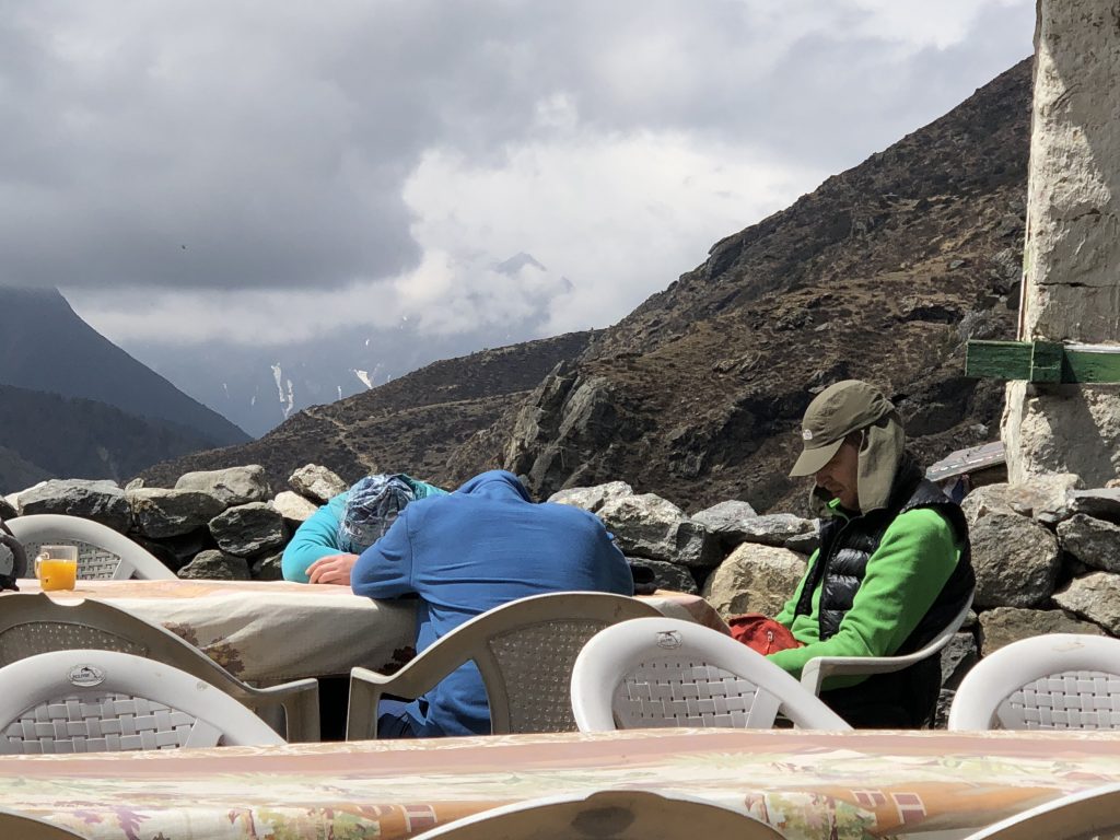 Three people slump over an outdoor table, their heads buried in their arms